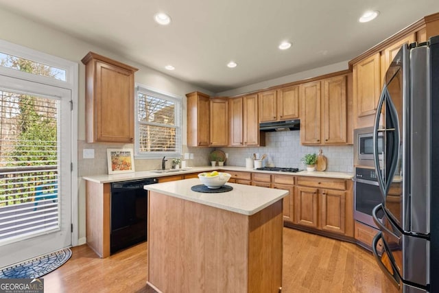 kitchen featuring under cabinet range hood, a sink, a kitchen island, light countertops, and appliances with stainless steel finishes