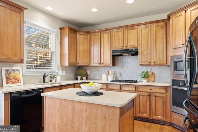 kitchen featuring light wood finished floors, a kitchen island, stainless steel appliances, under cabinet range hood, and a sink