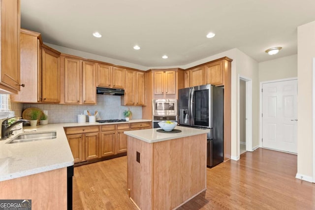 kitchen featuring under cabinet range hood, a kitchen island, a sink, appliances with stainless steel finishes, and backsplash