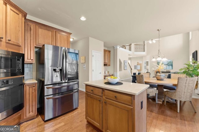 kitchen featuring appliances with stainless steel finishes, a center island, hanging light fixtures, an inviting chandelier, and light countertops