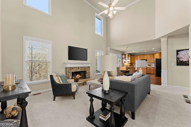 living area featuring visible vents, a ceiling fan, light carpet, a stone fireplace, and baseboards