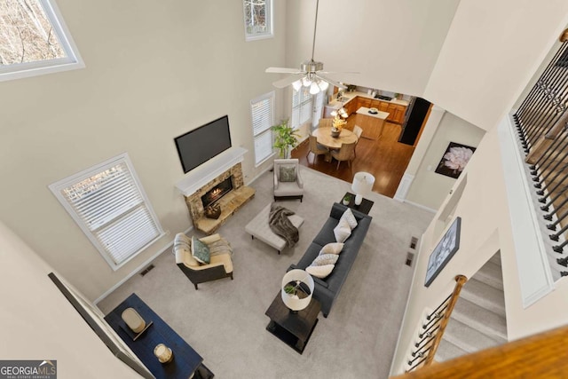 carpeted living room featuring visible vents, a towering ceiling, ceiling fan, stairway, and a fireplace