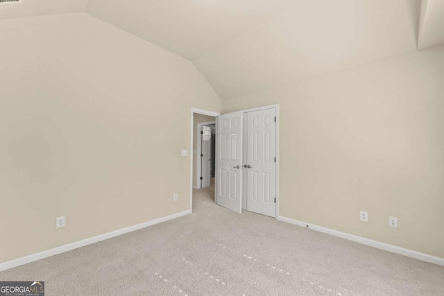 interior space with light carpet, vaulted ceiling, and baseboards