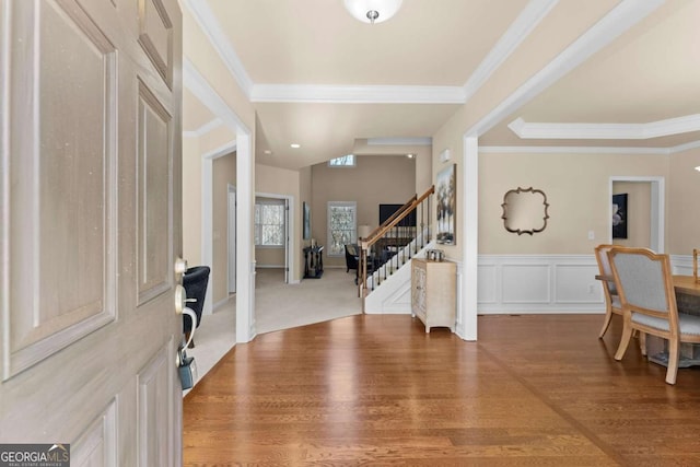 entrance foyer featuring crown molding, a decorative wall, stairway, wainscoting, and wood finished floors