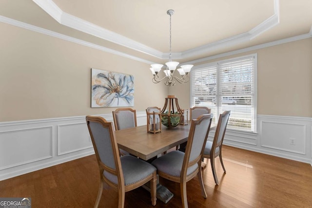 dining space featuring a raised ceiling, wainscoting, an inviting chandelier, and wood finished floors