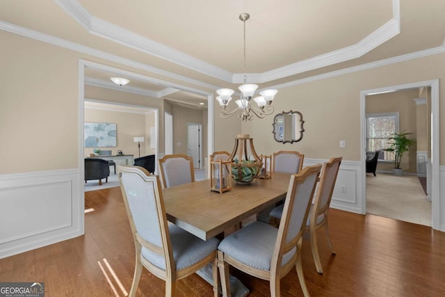 dining area with a tray ceiling, wainscoting, wood finished floors, and a notable chandelier