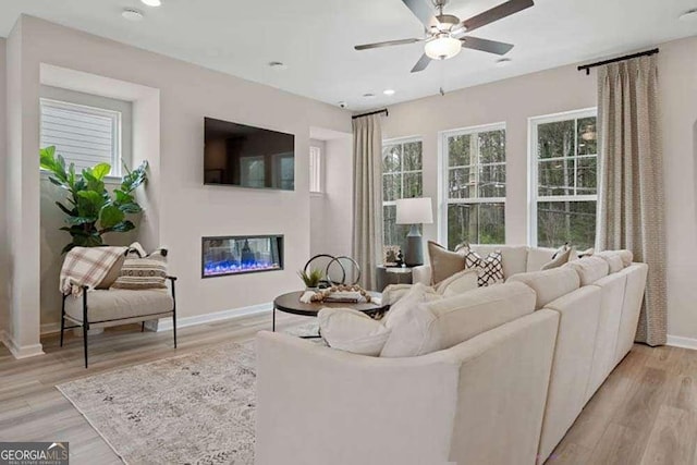 living room featuring baseboards, a glass covered fireplace, ceiling fan, light wood-style floors, and recessed lighting