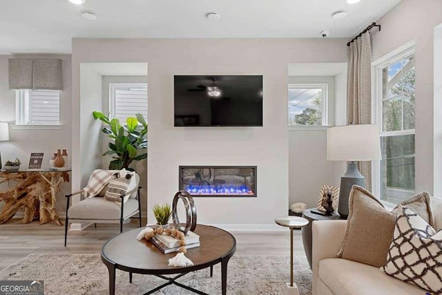 living room with light wood-type flooring, a glass covered fireplace, and baseboards