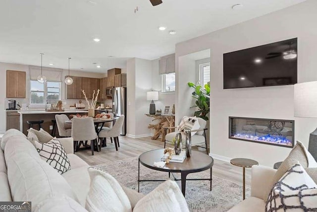 living area with ceiling fan, recessed lighting, baseboards, light wood finished floors, and a glass covered fireplace