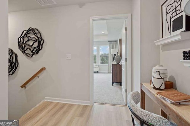 hallway with an upstairs landing, visible vents, light wood-style flooring, and baseboards