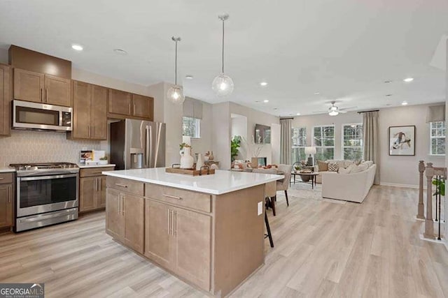 kitchen with a kitchen island, appliances with stainless steel finishes, open floor plan, light countertops, and pendant lighting