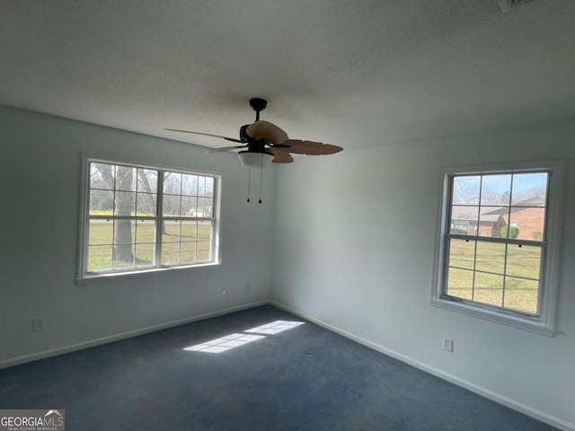 empty room featuring dark colored carpet, a healthy amount of sunlight, a textured ceiling, and baseboards