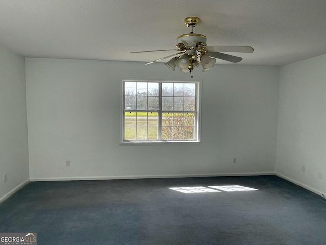 spare room featuring baseboards, dark carpet, and a ceiling fan