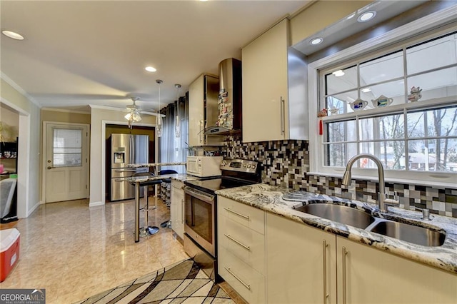 kitchen featuring light stone counters, stainless steel appliances, a sink, wall chimney range hood, and tasteful backsplash