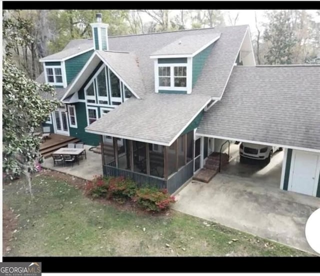 rear view of property featuring a patio, an attached carport, a shingled roof, a sunroom, and a yard