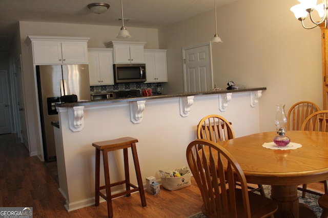 kitchen featuring stainless steel appliances, a breakfast bar, dark countertops, and white cabinetry