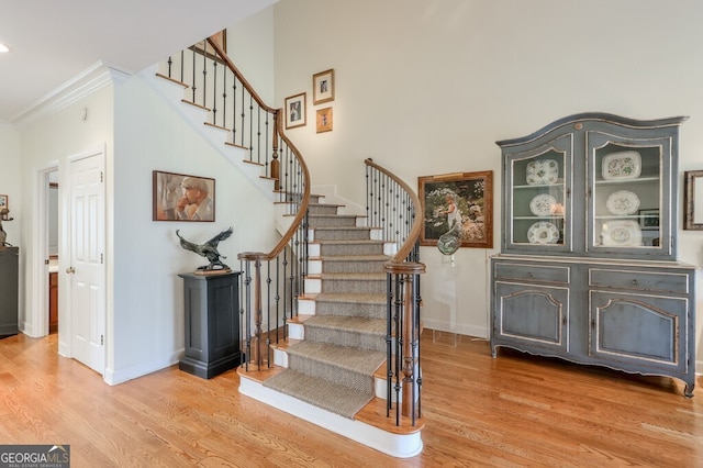 stairway with crown molding, a high ceiling, baseboards, and wood finished floors