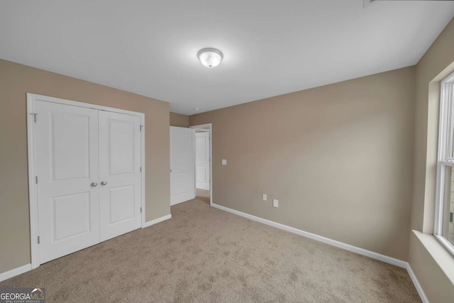 unfurnished bedroom with baseboards, a closet, and light colored carpet