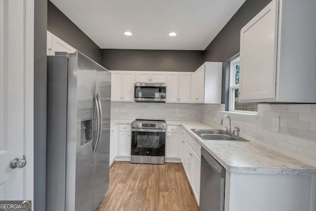 kitchen featuring white cabinets, light wood-style flooring, appliances with stainless steel finishes, light countertops, and a sink