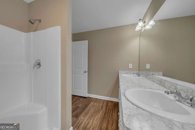 full bath featuring double vanity, a sink, baseboards, and wood finished floors