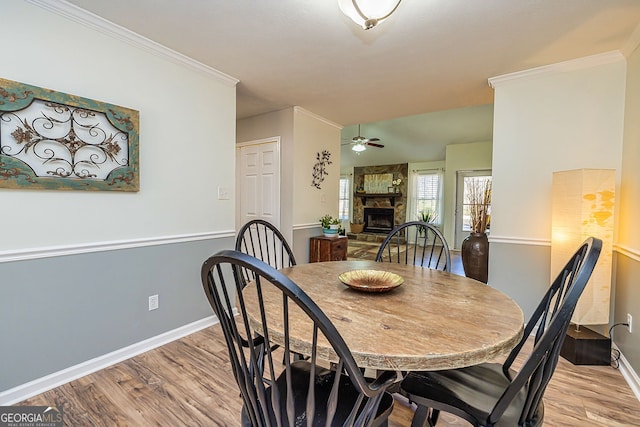 dining space with a fireplace, a ceiling fan, baseboards, light wood-type flooring, and crown molding