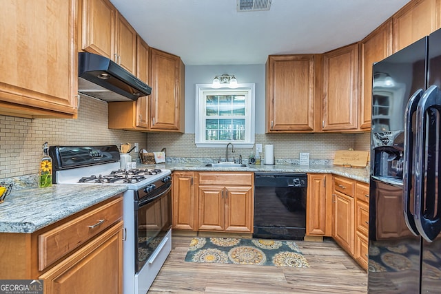 kitchen featuring light wood-style flooring, under cabinet range hood, a sink, black appliances, and tasteful backsplash