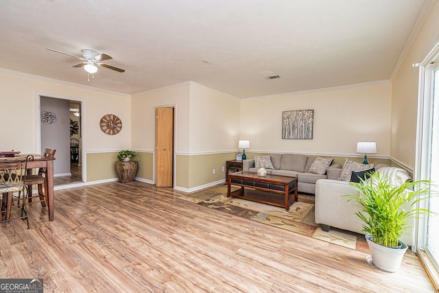 living area with light wood-style floors, baseboards, ornamental molding, and a ceiling fan