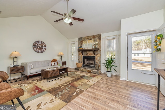 living area featuring ceiling fan, a stone fireplace, wood finished floors, high vaulted ceiling, and baseboards