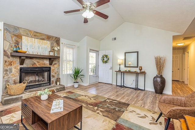 living area featuring vaulted ceiling, a stone fireplace, wood finished floors, and visible vents