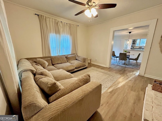 living area featuring a ceiling fan, baseboards, ornamental molding, and wood finished floors