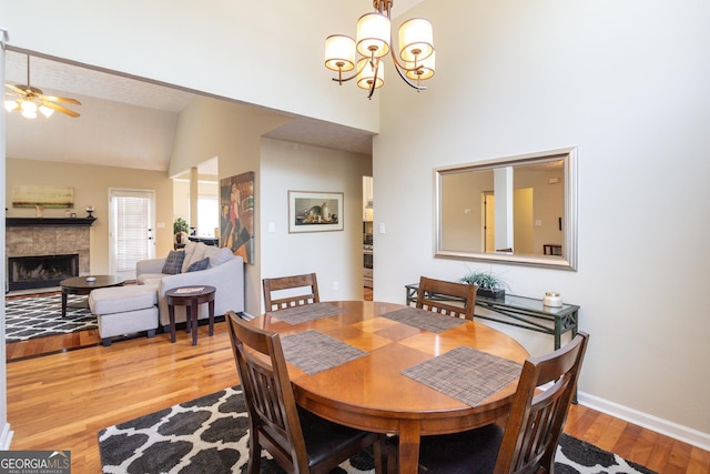 dining area featuring lofted ceiling, ceiling fan with notable chandelier, a fireplace, baseboards, and light wood finished floors