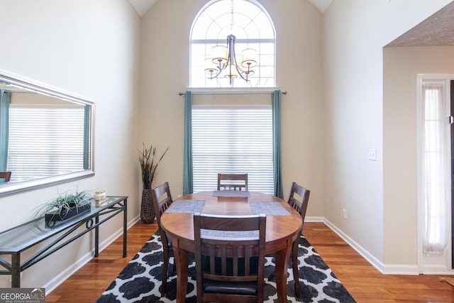 dining area featuring high vaulted ceiling, baseboards, a chandelier, and wood finished floors