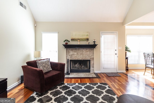 living room with a fireplace, visible vents, vaulted ceiling, and wood finished floors