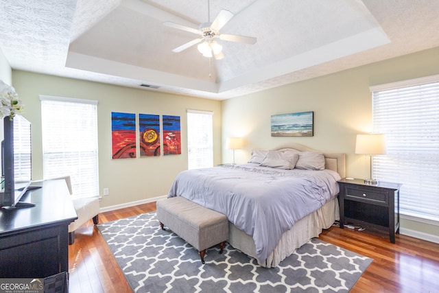 bedroom with a raised ceiling, multiple windows, baseboards, and wood finished floors