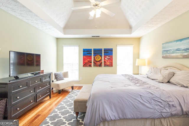 bedroom featuring a textured ceiling, ceiling fan, visible vents, light wood-style floors, and a raised ceiling