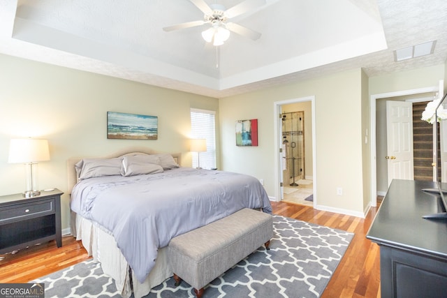 bedroom with baseboards, a raised ceiling, and light wood-style floors