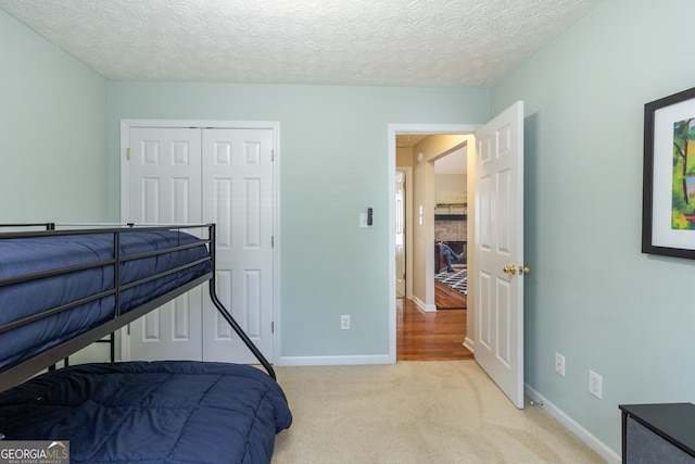 bedroom featuring baseboards, a textured ceiling, a closet, and light colored carpet