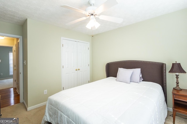 bedroom featuring baseboards, a ceiling fan, light colored carpet, a textured ceiling, and a closet