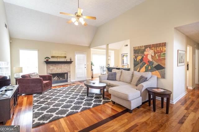 living area featuring baseboards, a tile fireplace, lofted ceiling, ceiling fan, and wood finished floors