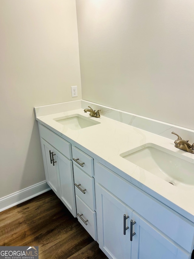 bathroom with double vanity, wood finished floors, a sink, and baseboards