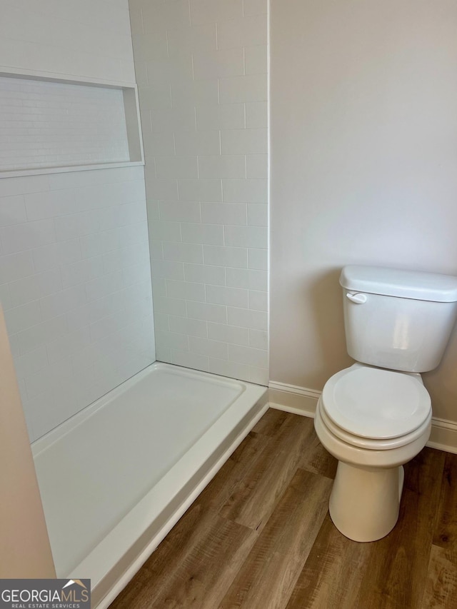 full bathroom featuring baseboards, a tile shower, toilet, and wood finished floors