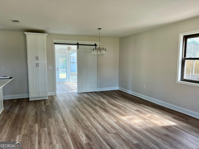 unfurnished dining area featuring light wood finished floors, a barn door, visible vents, and baseboards