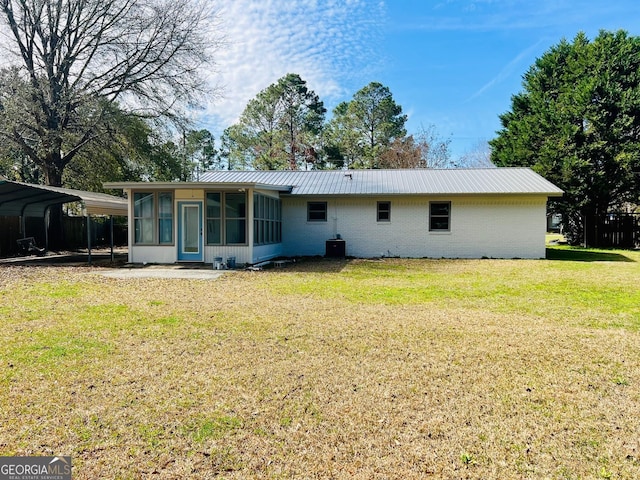 back of property with brick siding, a detached carport, a lawn, a sunroom, and metal roof