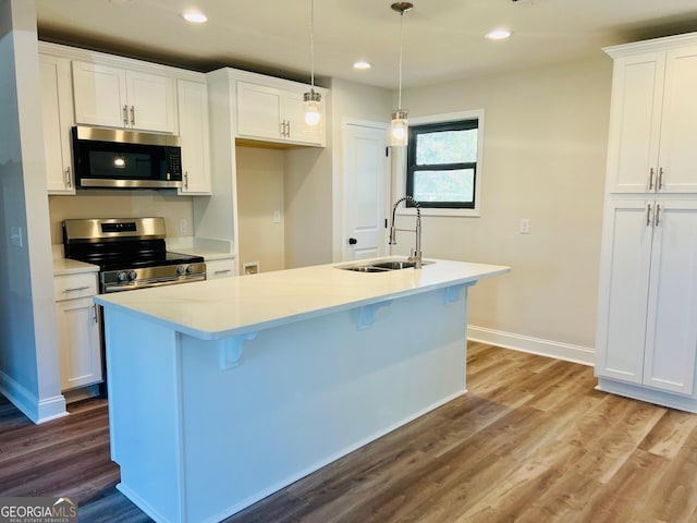 kitchen featuring stainless steel appliances, a sink, white cabinetry, light countertops, and a center island with sink