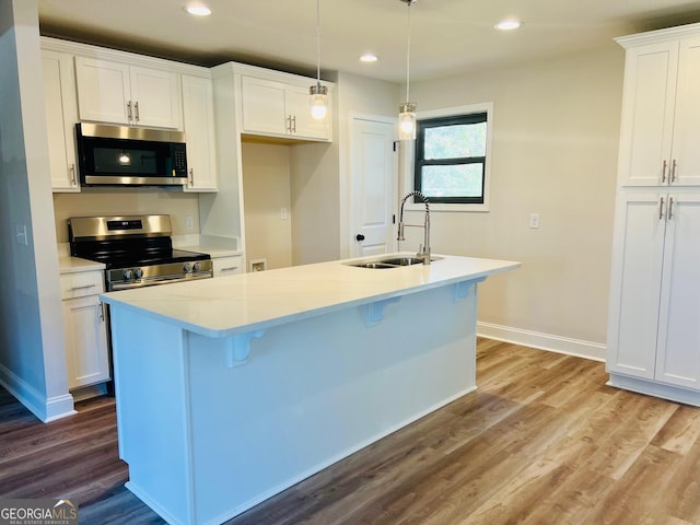 kitchen featuring white cabinets, stainless steel appliances, a sink, and an island with sink