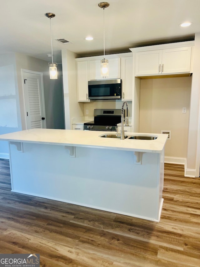 kitchen with stainless steel appliances, white cabinets, light countertops, an island with sink, and pendant lighting