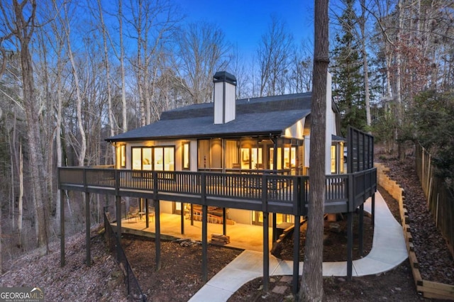 back of house with a patio area, a chimney, a deck, and roof with shingles