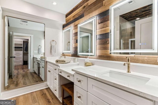 full bath featuring double vanity, visible vents, a stall shower, a sink, and wood finished floors