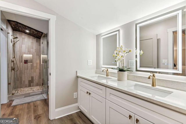 bathroom featuring double vanity, wood finished floors, a stall shower, and a sink