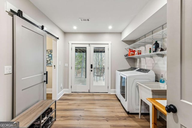 laundry area with washer and dryer, visible vents, a barn door, light wood-type flooring, and laundry area
